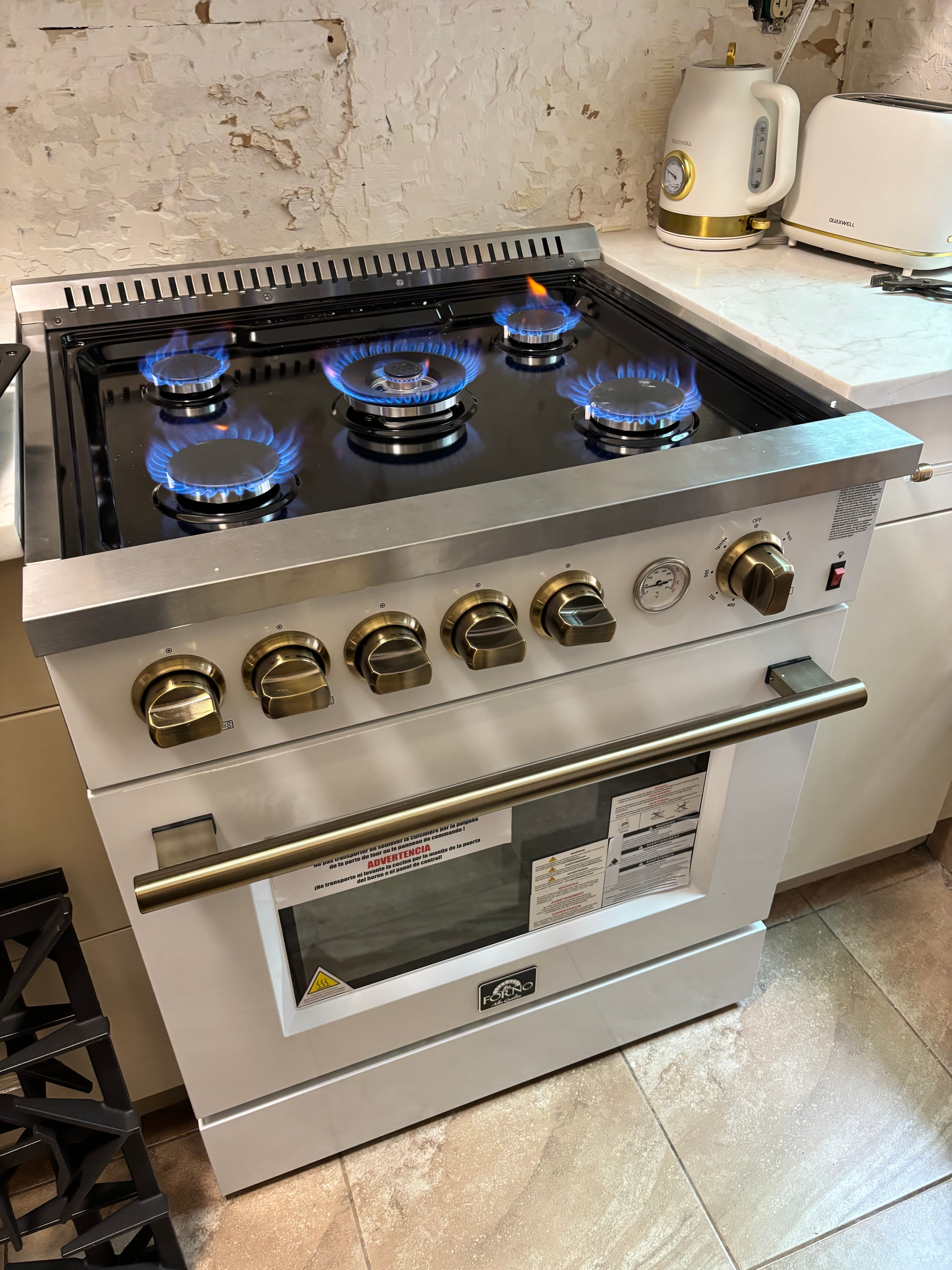 White gas range with five lit blue burners, brass knobs, and a matching oven handle.