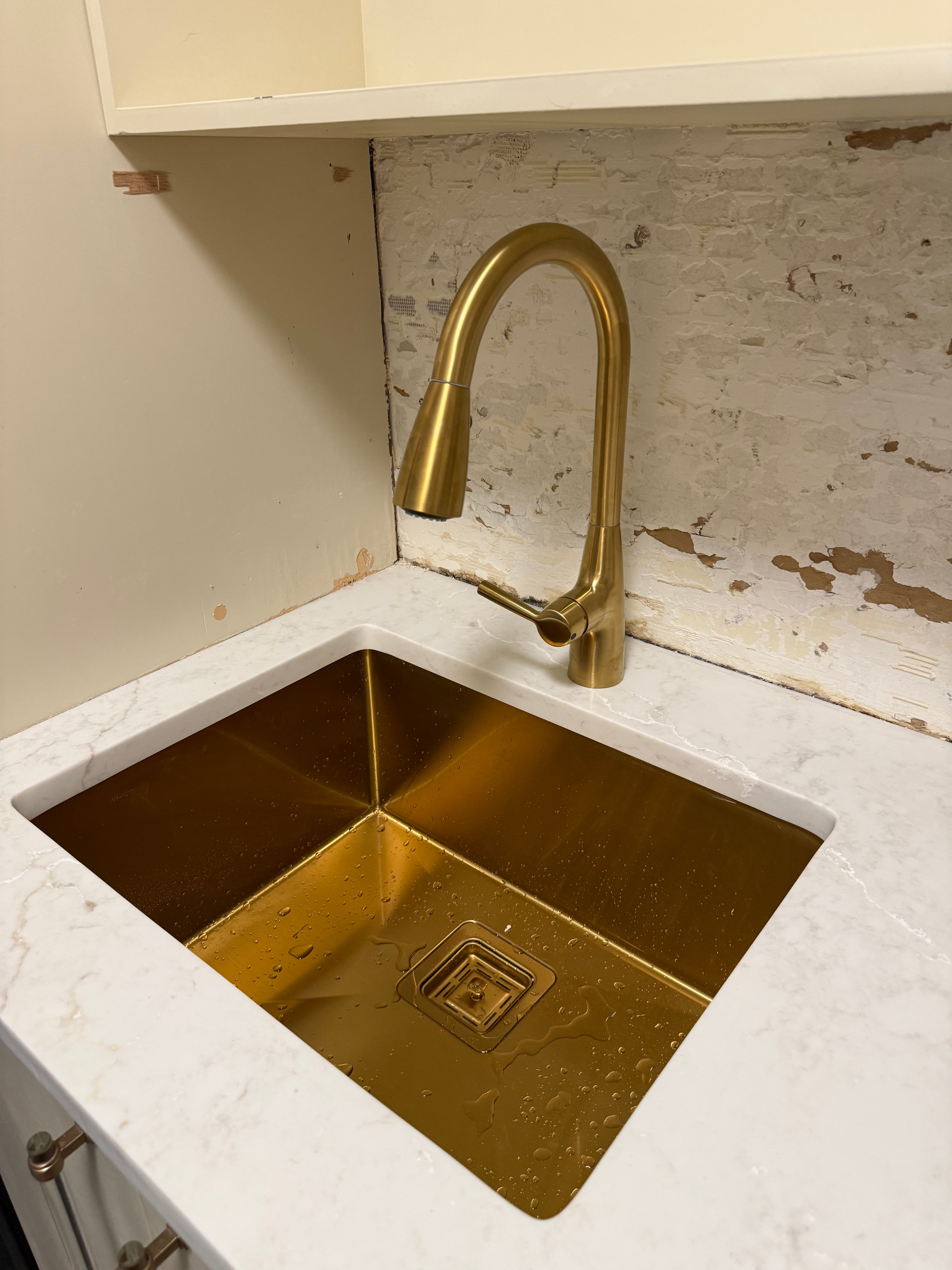 Gold rectangular undermount sink and matching gooseneck faucet on a white marble-patterned countertop.