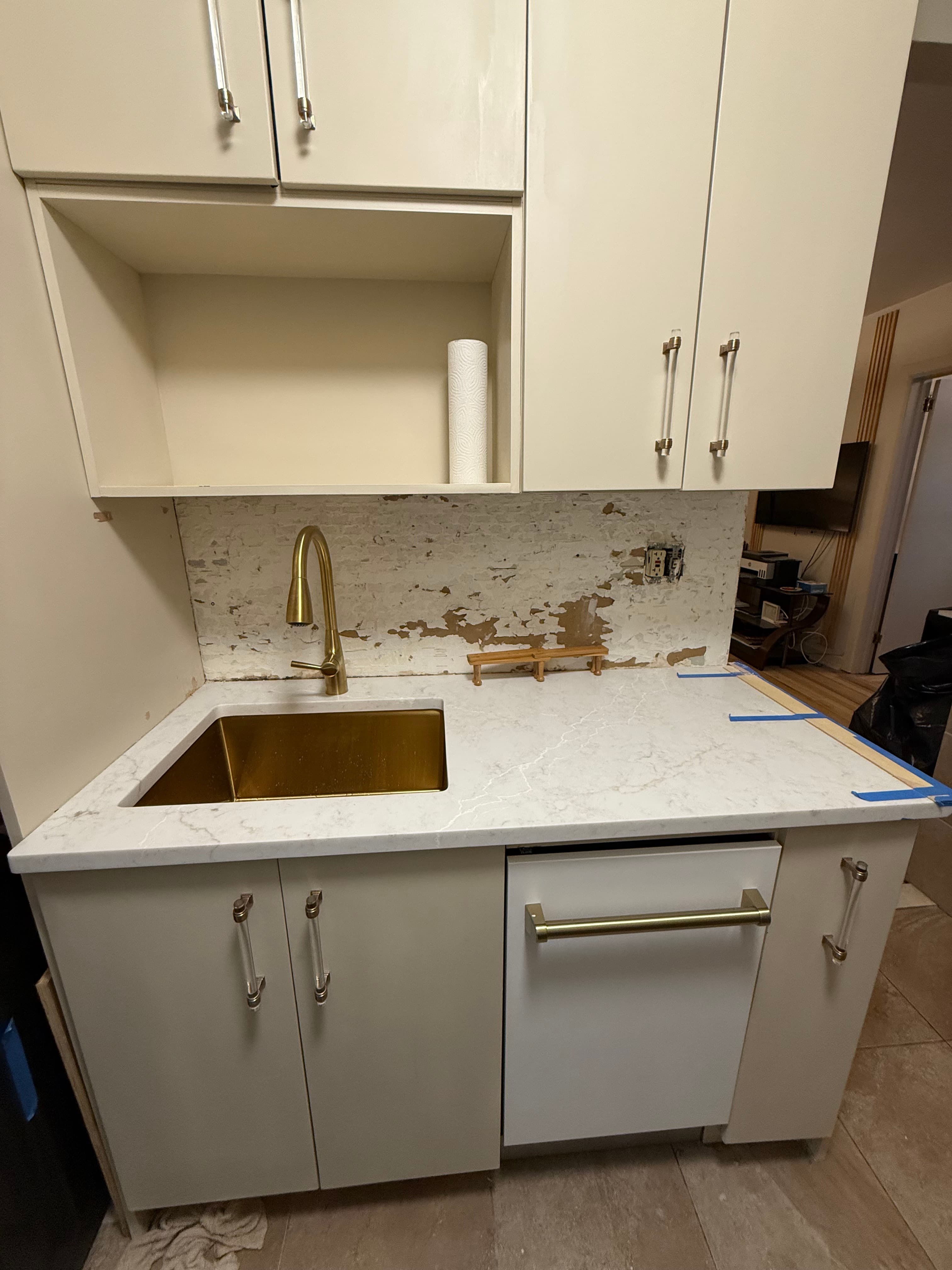 Gold sink and faucet in white marble countertop with unfinished backsplash during a kitchen remodel.