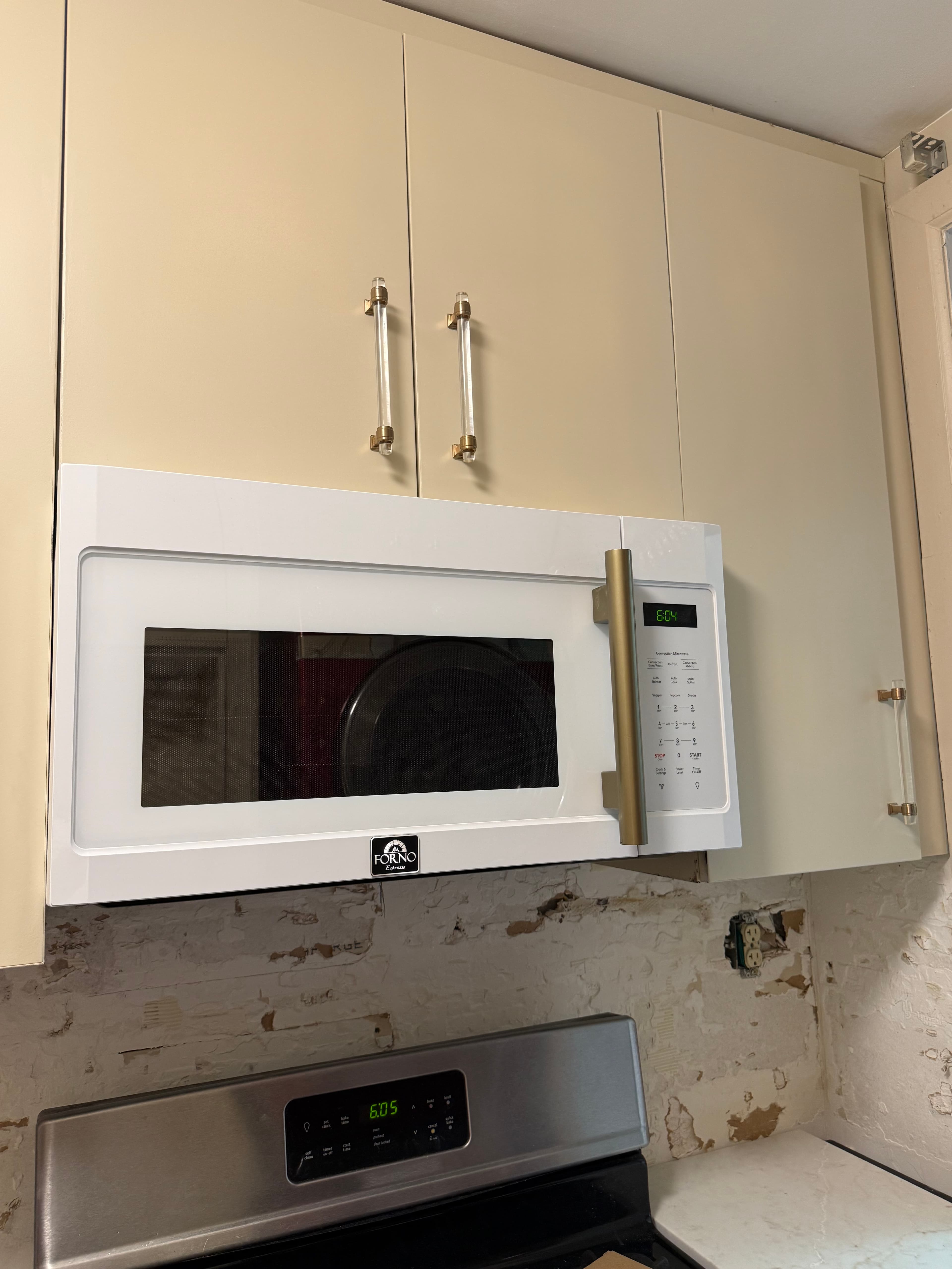 White microwave with gold handle installed above a stainless stove against an unfinished kitchen wall.
